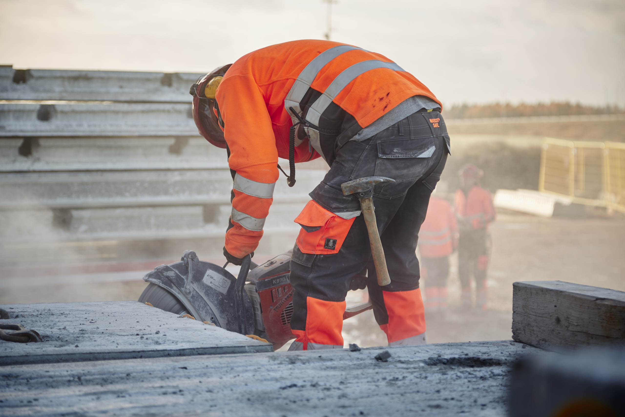 Arbeiter in orangener Arbeitskleidung der mit einer Kreissäge arbeitet.