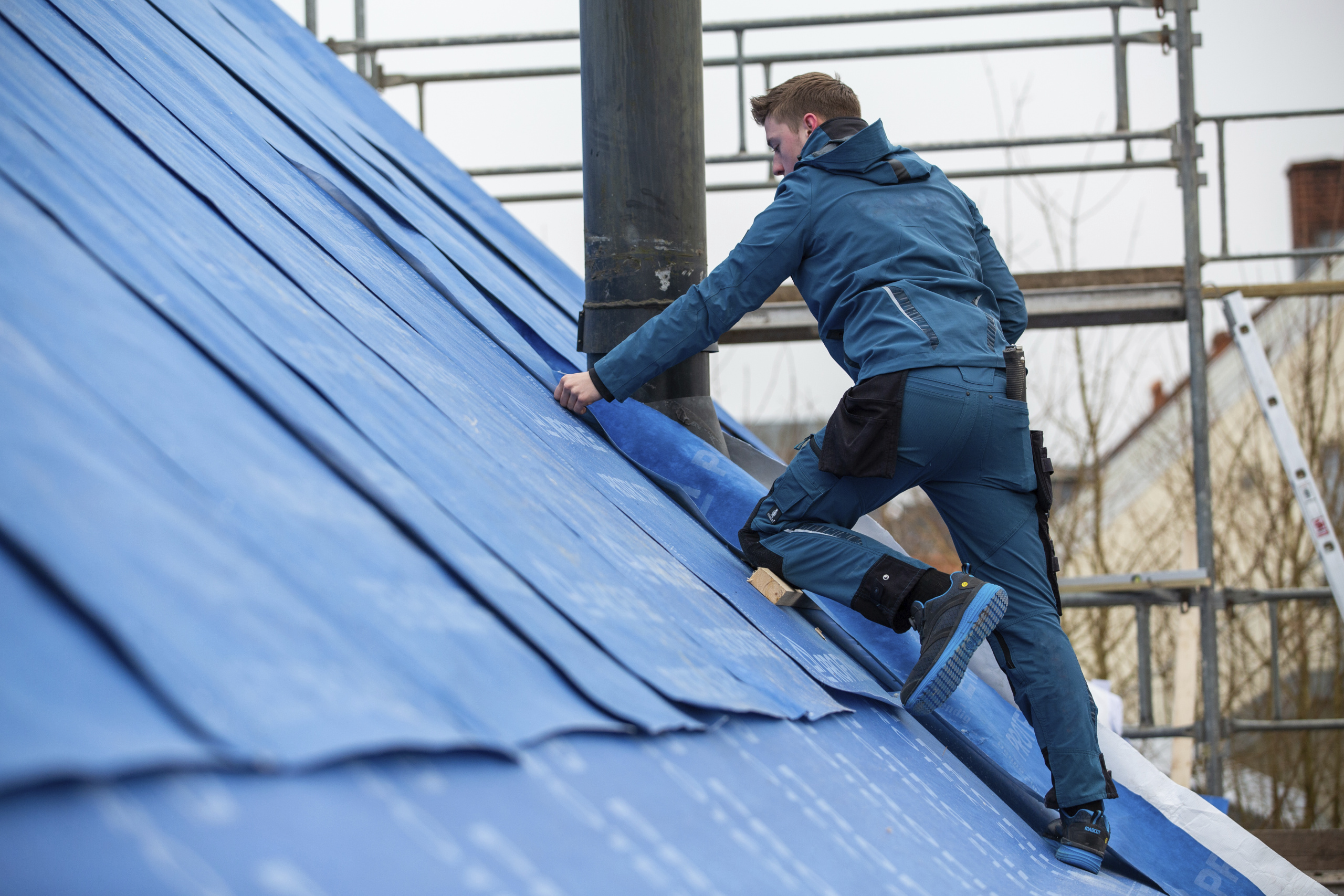 Dachdecker in blauer Arbeitskleidung der Plastikversiegelung auf dem Dach montiert.
