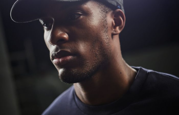 Mann mit einer schwarzen Kappe und einem gebogenen Schild. Auf der Front ist ein zweifarbiges Embleme eingestickt.